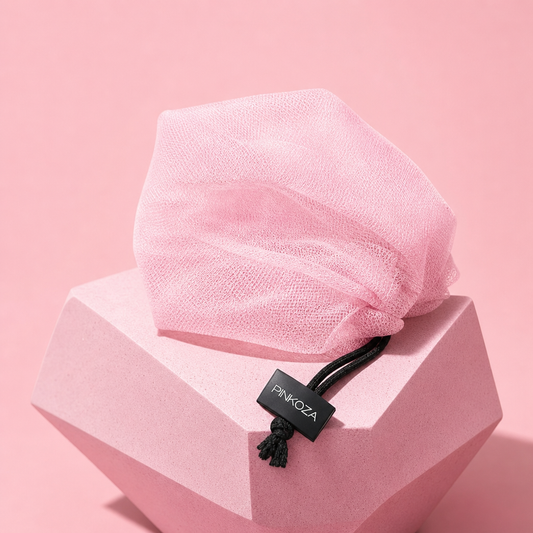 PINKOZA pink mesh soap bag with black drawstring tag resting on a geometric pink pedestal