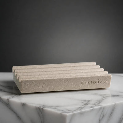 PINKOZA The Dry Stone soap dish featuring a textured stone finish, sloped ridges, and an engraved logo resting on a white marble surface.